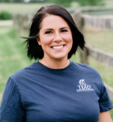 Melissa smiling with a TEAD shirt in front of a paddock