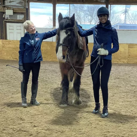 A rider and volunteer standing with Willy in our indoor arena, smiling at the camera!