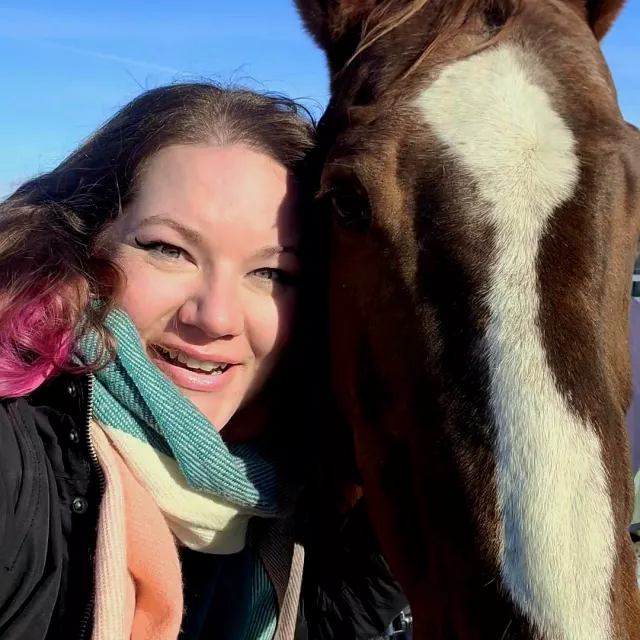 A close up photo of Kris smiling at the camera, with Lady, a chestnut TEAD horse, beside her. 